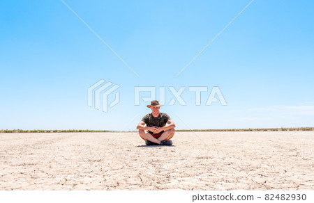 a man with a hat sits on dry, cracked ground a man with a hat sits on dry, cracked ground 82482930