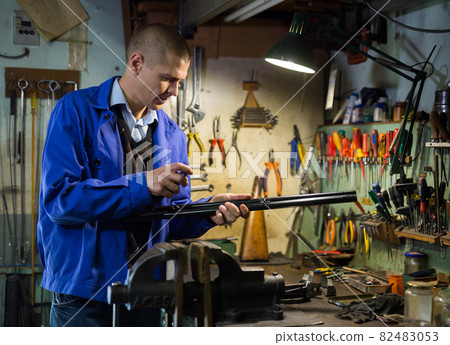 Professional craftsman repairing and assembling shotgun in weapons workshop 82483053
