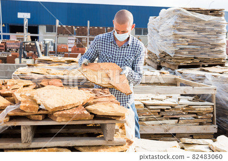 Man supervisor in mask checking quality of natural stone tiles 82483060