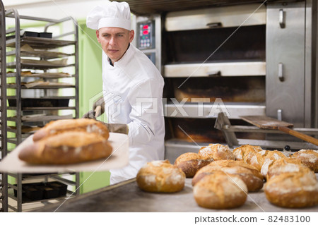 man in chefs uniform with bread on shovel in bakehouse 82483100
