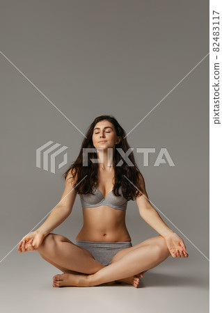 Young adorable woman in lingerie sitting on floor isolated over gray studio background. Natural beauty concept. 82483117