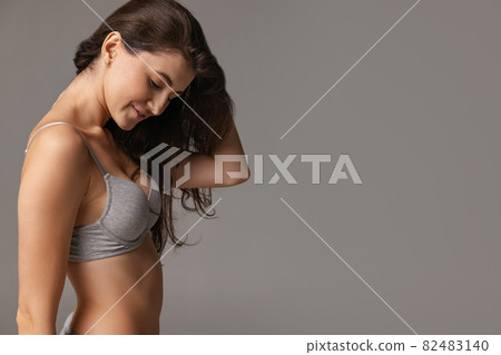 Half-length portrait of young beautiful slim woman in lingerie isolated over gray studio background. Natural beauty concept. Half-length portrait of young beautiful slim woman in lingerie isolated over gray studio background. Natural beauty concept. 82483140