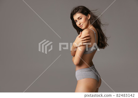 Half-length portrait of young beautiful slim woman in lingerie isolated over gray studio background. Natural beauty concept. Half-length portrait of young beautiful slim woman in lingerie isolated over gray studio background. Natural beauty concept. 82483142