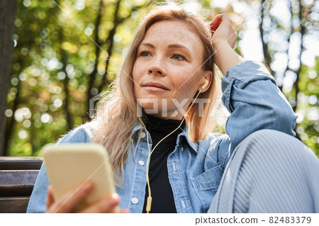 Happy girl looking away and listening music at her smartphone at the park 82483379