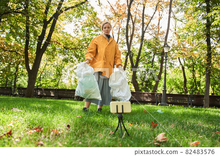 Volunteer woman standing with bag while picking up trash at the park Volunteer woman standing with bag while picking up trash at the park 82483576