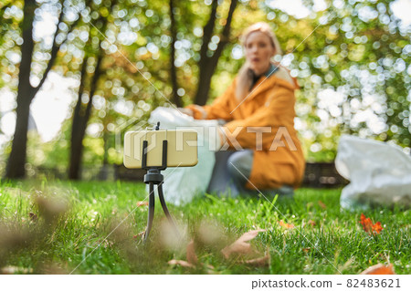 Volunteer woman crouching with bag while picking up trash at the park Volunteer woman crouching with bag while picking up trash at the park 82483621