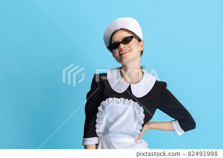 Young woman in chambermaid uniform and stylish sunglasses isolated over blue background 82491998