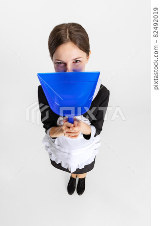 Pretty young girl in cleaning uniform hiding face behind dustpan isolated over white background Pretty young girl in cleaning uniform hiding face behind dustpan isolated over white background 82492019