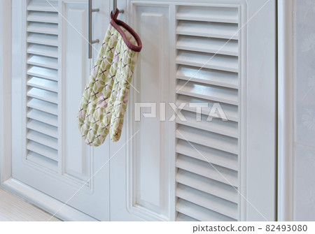 The heat-resistant gloves in the leaf pattern is hanging on the handle of the cabinet. 82493080