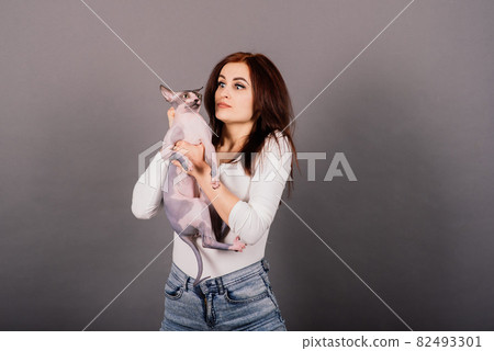Young woman with canadian sphynx cat in studio, grey background Young woman with canadian sphynx cat in studio, grey background 82493301