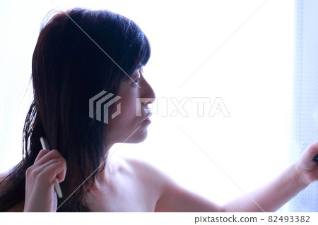 A woman looking in the mirror and messing with her hair 82493382