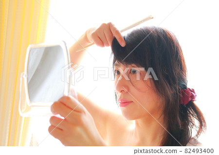 A woman looking in the mirror and messing with her hair 82493400