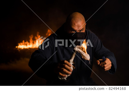 A masked man is holding a burning bottle. Molotov cocktail. A masked man is holding a burning bottle. Molotov cocktail. 82494168