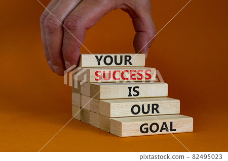 Your success is our goal symbol. Wooden blocks with words 'your success is our goal'. Businessman hand. Beautiful orange background, copy space. Success business goal concept. Your success is our goal symbol. Wooden blocks with words 'your success is our goal'. Businessman hand. Beautiful orange background, copy space. Success business goal concept. 82495023