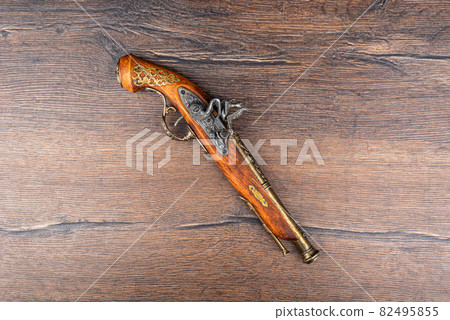 Mock up of an old pistol with bronze inlay on a wooden background. Mock up of an old pistol with bronze inlay on a wooden background. 82495855