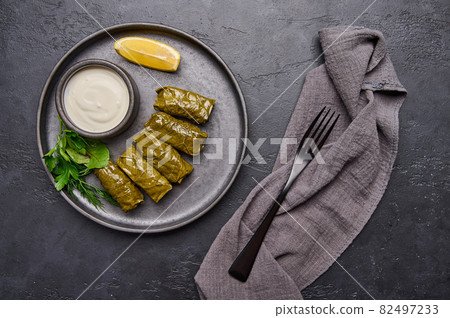 Top view dolma, parsley, saucepan with sour cream and lemon in black plate on dark table Top view dolma, parsley, saucepan with sour cream and lemon in black plate on dark table 82497233