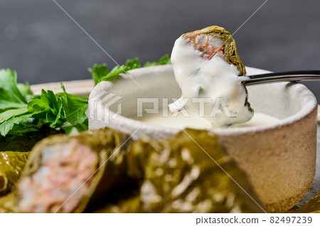 Piece of dolma with sour cream on black fork over the saucepan Piece of dolma with sour cream on black fork over the saucepan 82497239