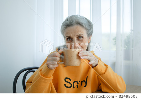 Elderly gray-haired woman is drinking coffee while sitting at home. Happy retirement Elderly gray-haired woman is drinking coffee while sitting at home. Happy retirement 82498505