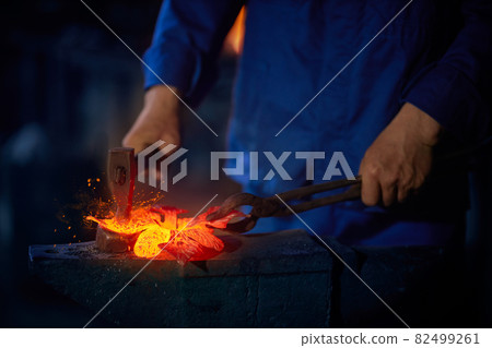 Man using pliers and hammer while working with molten metal 82499261