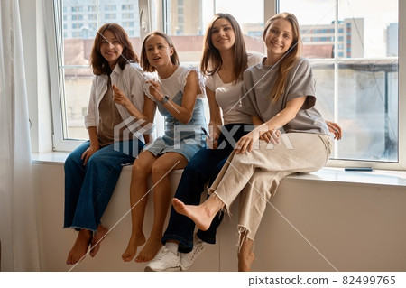 Girls having fun on window sill. Four caucasian girls sitting on window sill discuss something and Girls having fun on window sill. Four caucasian girls sitting on window sill discuss something and 82499765