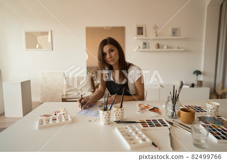 Beautiful Female Artist In Her Studio. Female drawing in album with watercolor paints and paintbrush Beautiful Female Artist In Her Studio. Female drawing in album with watercolor paints and paintbrush 82499766