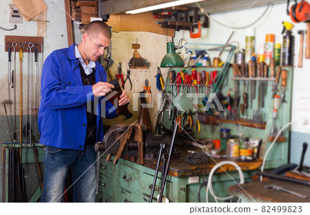 Professional craftsman repairing and assembling shotgun in weapons workshop Professional craftsman repairing and assembling shotgun in weapons workshop 82499823