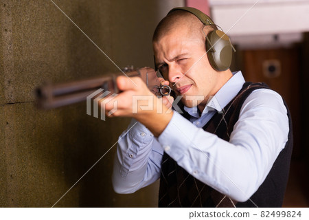 Concentrated man practicing shotgun shooting at firing range Concentrated man practicing shotgun shooting at firing range 82499824