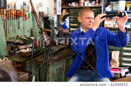 Professional craftsman adjusting optical sight in weapons workshop 82499852