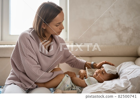 Young little boy on the sofa with cooler gel on her head and measuring temperature by thermometer Young little boy on the sofa with cooler gel on her head and measuring temperature by thermometer 82500741