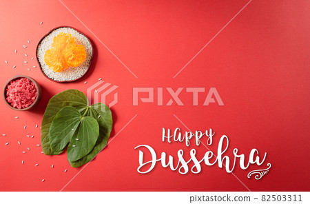 Happy Dussehra. Yellow flowers, green leaf and rice on red background. Dussehra Indian Festival concept. 82503311