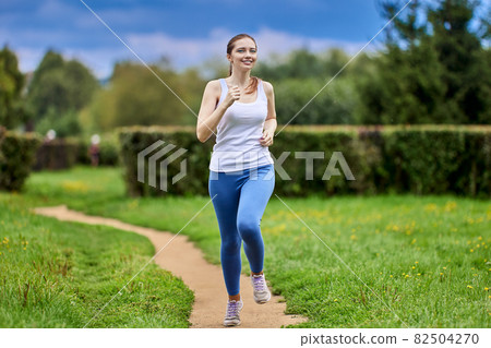 White slim woman runs in public park in sportswear. White slim woman runs in public park in sportswear. 82504270