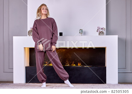Happy white woman 26 years old stands near fireplace in living room. Happy white woman 26 years old stands near fireplace in living room. 82505305