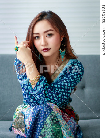 Young, beautiful cute Asian girl, dressed in gypsy style casually clothes with self-confident manner, sitting on the sofa and looking at the camera 82508632