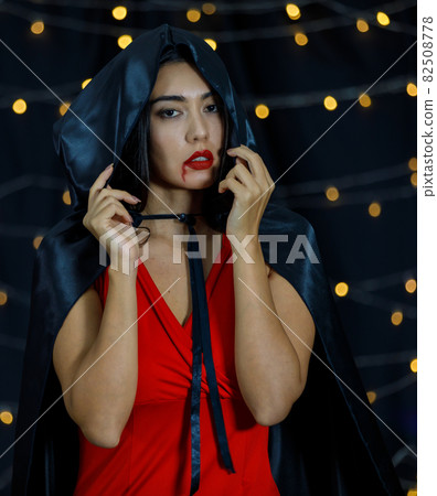 Gothic woman in black cape with blood on lips Gothic woman in black cape with blood on lips 82508778