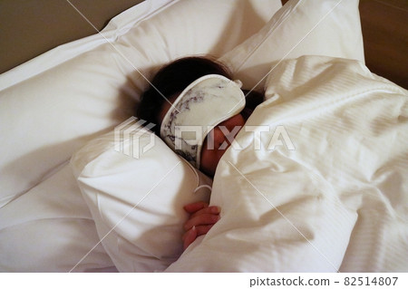 帶著眼罩睡覺的女人躺在白色床鋪蓋著白色的棉被 82514807