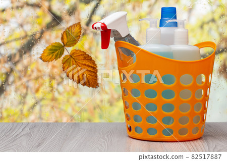 Bottles of dishwashing liquid in a plastic basket in front of the window with water drops. Bottles of dishwashing liquid in a plastic basket in front of the window with water drops. 82517887