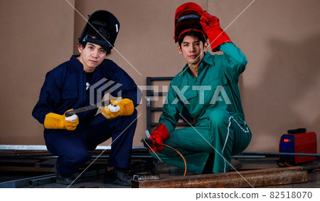 young smart Asian sitting and posing to a camera for photographing in a factory. They are wearing a safety outfit for factory working with a mechanic jumpsuit, glove, boots, and welding helmet young smart Asian sitting and posing to a camera for photographing in a factory. They are wearing a safety outfit for factory working with a mechanic jumpsuit, glove, boots, and welding helmet 82518070