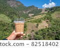 Hand holding a glass of cold espresso coffee Background blurry views tree and mountain 82518402