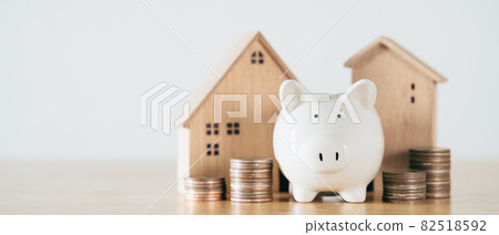 Wooden house with white piggy bank and stacking coins on wooden table. saving money for buying house, financial plan home loan concept. Wooden house with white piggy bank and stacking coins on wooden table. saving money for buying house, financial plan home loan concept. 82518592