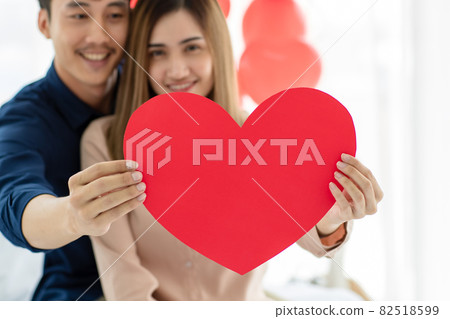 Happy Asian couple with heart sitting on bed Happy Asian couple with heart sitting on bed 82518599