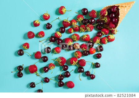 Berries in waffle cone - strawberry and black cherry on blue bac Berries in waffle cone - strawberry and black cherry on blue bac 82521084
