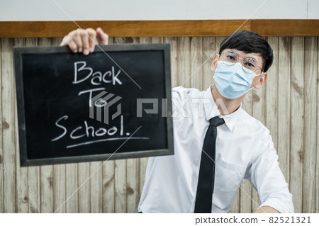Back to school. Asian male students wearing masks, holding blackboard labeled Back to School. College male Back to School after Pandemic Coronavirus Disease 2019 82521321