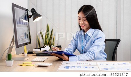 Asian women sit at their desks and calculate financial graphs showing results about their investments, plan a successful business growth process 82521847