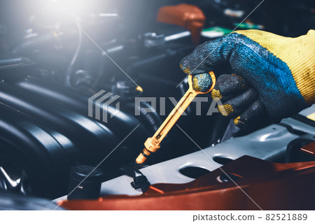 Mechanic hand pulling up oil dipstick of the car engine for checking oil level Mechanic hand pulling up oil dipstick of the car engine for checking oil level 82521889