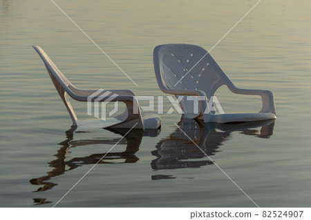 plastic white chairs in the water near the shore on the beach 82524907