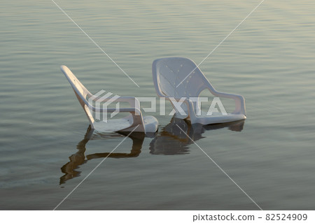 plastic white chairs in the water near the shore on the beach 82524909