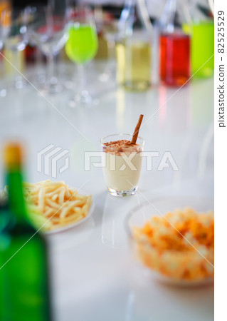 Tasty creamy spiced homemade eggnog drink with gingerbread in glass on middle of beverages table in Thanksgiving Christmas eve party surrounded by other alcoholic bottles liquor fries and snacks Tasty creamy spiced homemade eggnog drink with gingerbread in glass on middle of beverages table in Thanksgiving Christmas eve party surrounded by other alcoholic bottles liquor fries and snacks 82525529