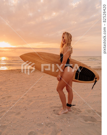 Young surfer woman with surfboard on beach and warm sunrise. Young surfer woman with surfboard on beach and warm sunrise. 82526420