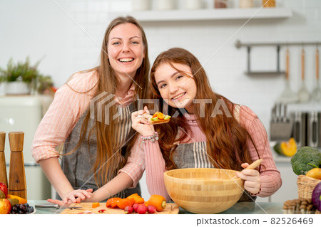 Young daughter hold spoon with mixed vegetable and look at camera with smiling and stay with mother 82526469