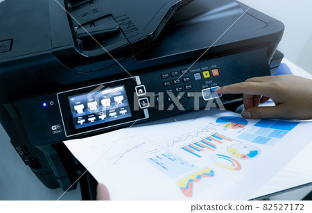 Office worker prints paper on multifunction laser printer. Copy, print, scan, and fax machine in office. Document and paper work. Print technology. Hand press on photocopy machine. Scanner equipment. 82527172